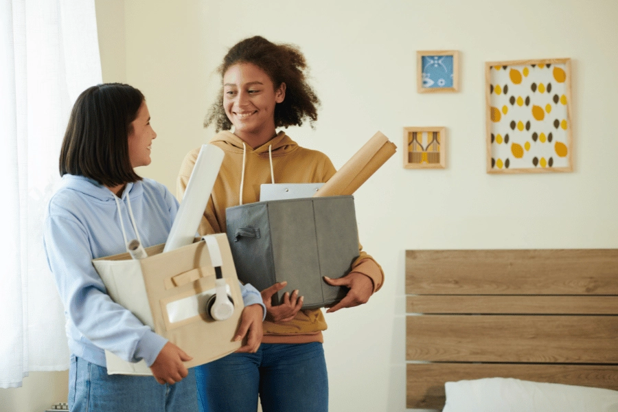 two girl roommates moving in together holding boxes of their belongings